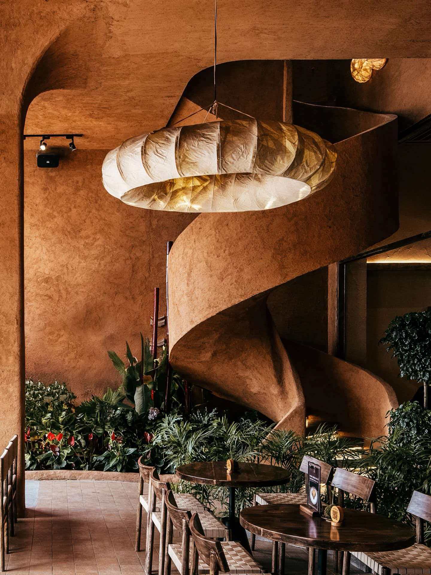 Restaurant with sculptural spiral staircase, terracotta plaster walls and pendant lighting